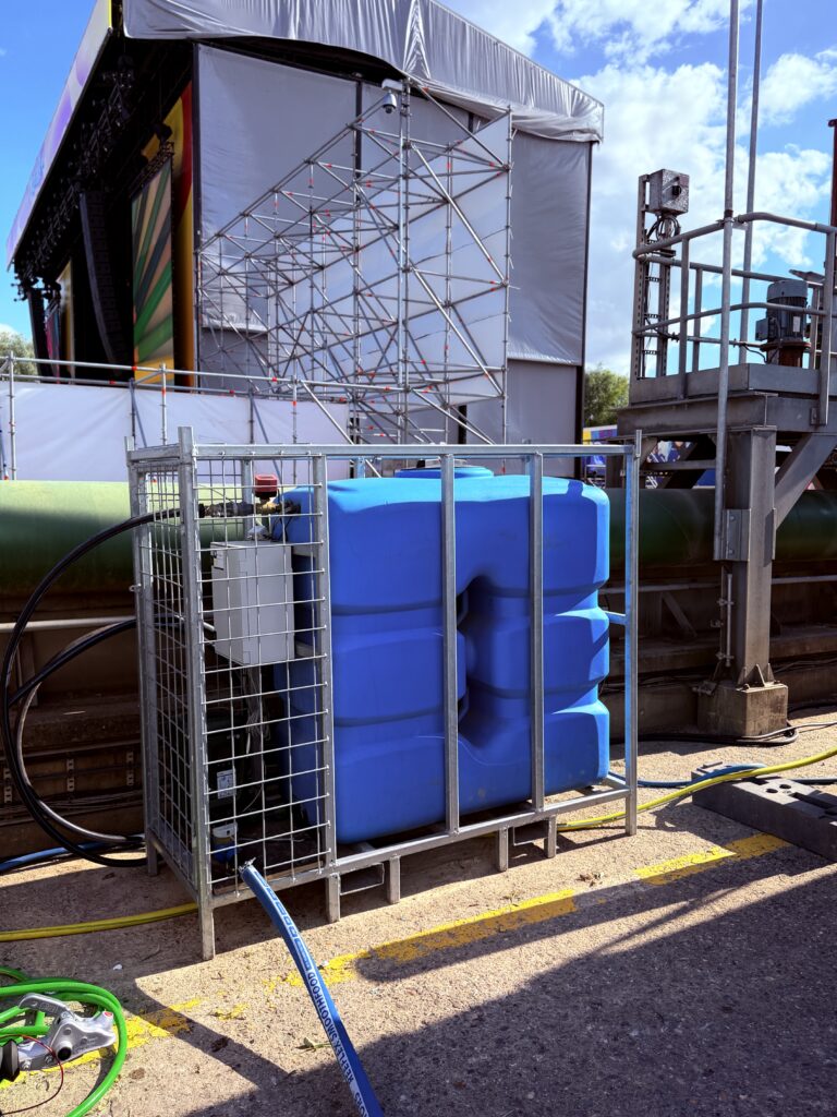 Watervat met drukset en sturingskast in één frame, opgesteld naast een festivalpodium