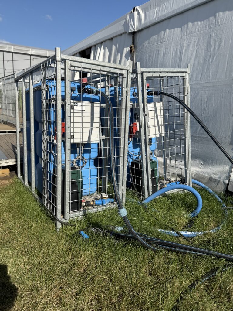 Blauwe watervaten in thermisch verzinkte transportframes naast een festivaltent